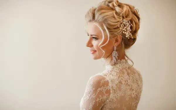Elegancka panna młoda z perłowymi ozdobami ślubnymi do włosów i kryształowymi kolczykami.